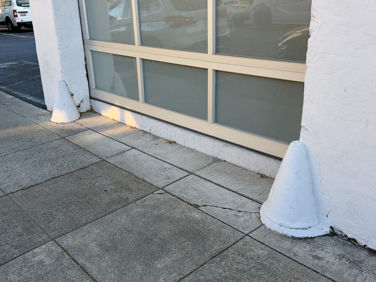 Two cone-shaped white bollards guarding a storefront's glass entrance on a sidewalk.