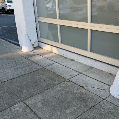 Two cone-shaped white bollards guarding a storefront's glass entrance on a sidewalk.