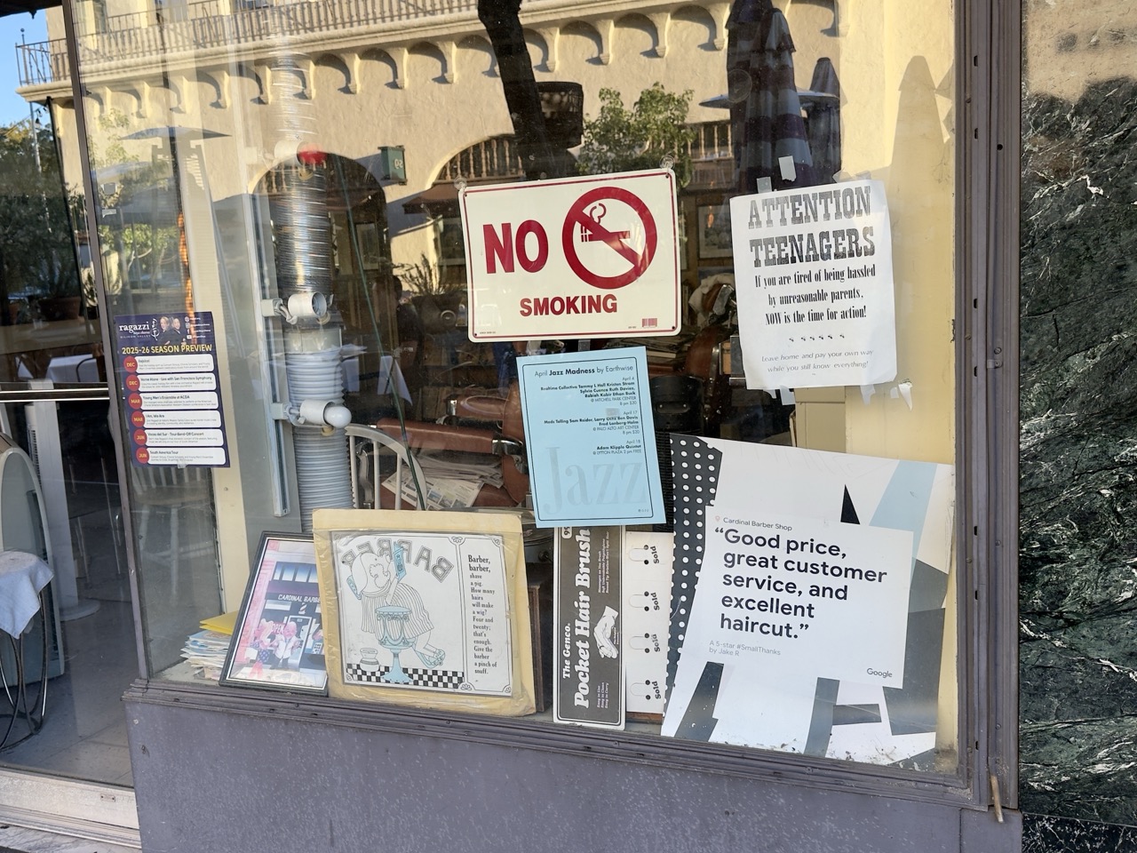A barbershop window covered in signs, including a no-smoking notice and a tongue-in-cheek 'Attention Teenagers' flyer.