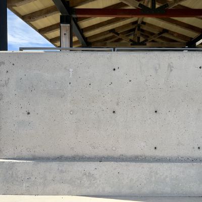 A large concrete pillar beneath a park pavilion's peaked roof, with a tiny stick-figure drawing near its top.