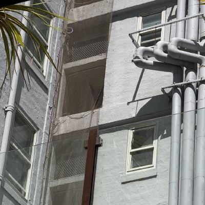 Large gray exhaust pipes running up the side of a stucco building, framed by a palm tree