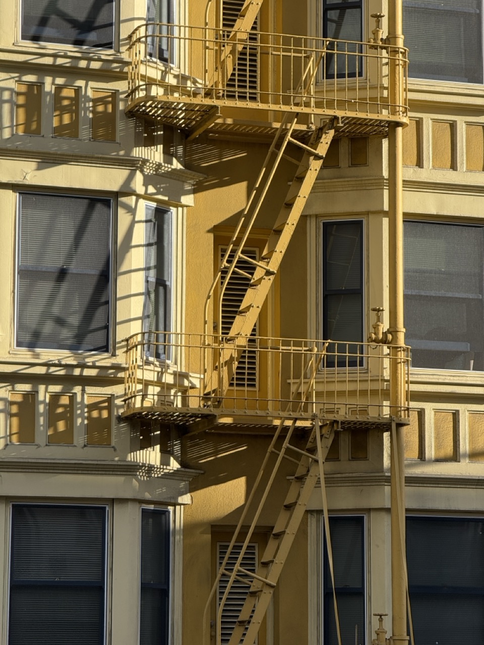 A yellow apartment building's exterior fire escape zigzagging past shuttered windows