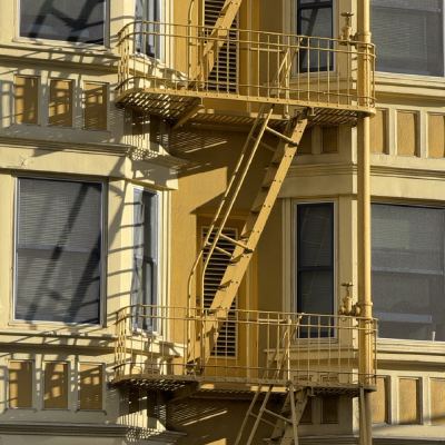 A yellow apartment building's exterior fire escape zigzagging past shuttered windows