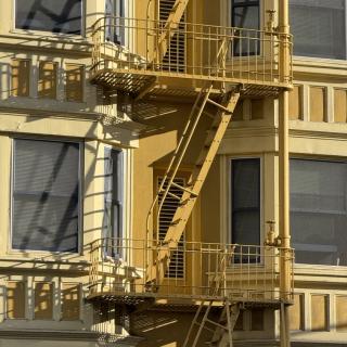 A yellow apartment building's exterior fire escape zigzagging past shuttered windows