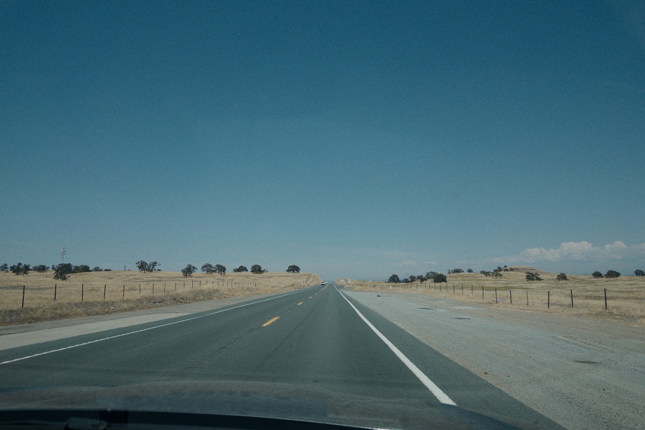 An empty two-lane highway through dry golden hills, shot from inside a moving car