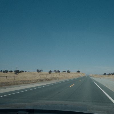 An empty two-lane highway through dry golden hills, shot from inside a moving car