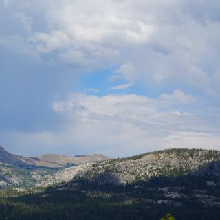 A rain shaft falling from dark clouds over a ridge of granite peaks and forest