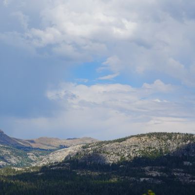 A rain shaft falling from dark clouds over a ridge of granite peaks and forest