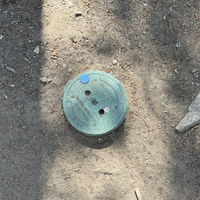 A round green irrigation control valve cover set into bare dirt