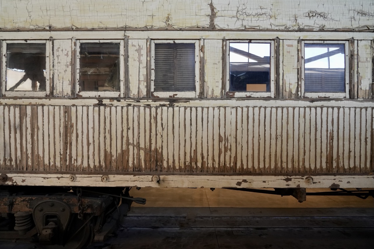 The weathered exterior of an old wooden train car, its white paint peeling to bare wood