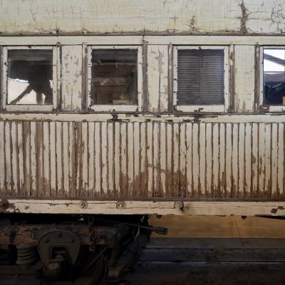 The weathered exterior of an old wooden train car, its white paint peeling to bare wood