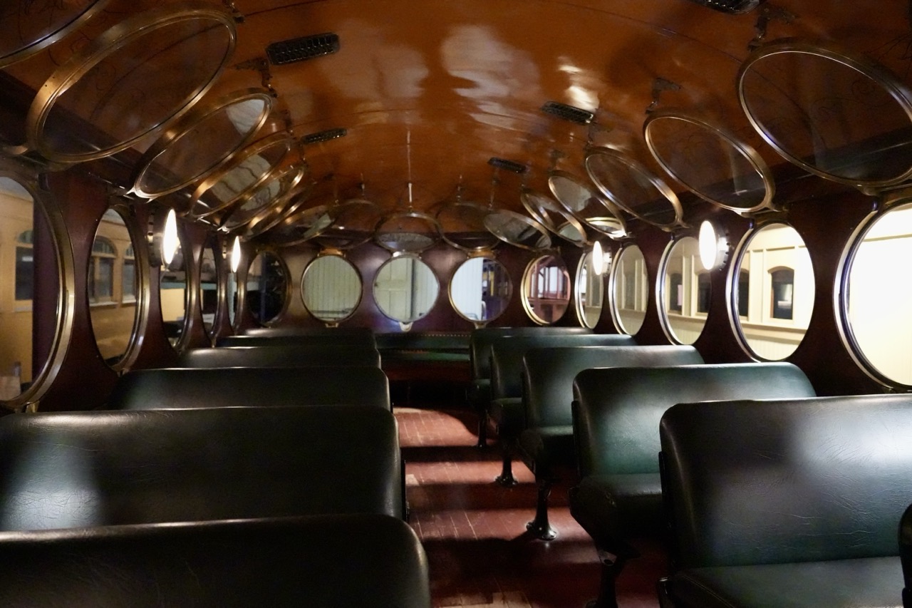 The interior of a vintage train car, rows of green leather seats beneath oval windows