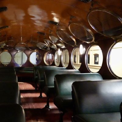 The interior of a vintage train car, rows of green leather seats beneath oval windows