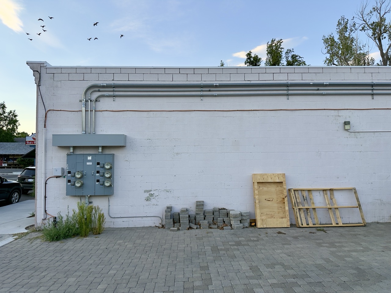 The back of a cinderblock building with an electrical meter panel and wooden pallets leaning against the wall