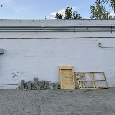 The back of a cinderblock building with an electrical meter panel and wooden pallets leaning against the wall