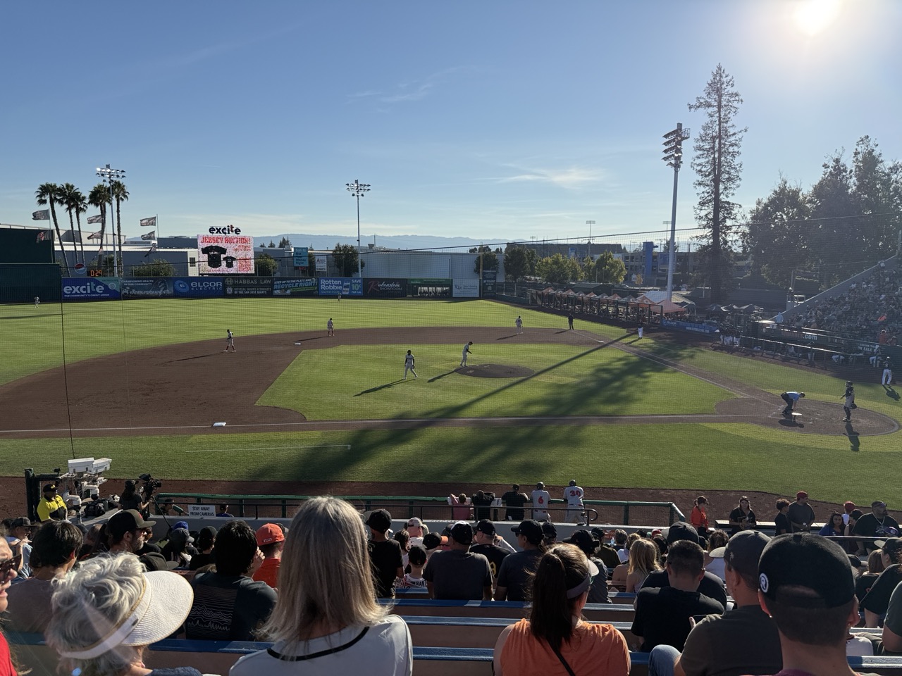 A minor-league baseball game in progress, seen from the stands with players on the infield
