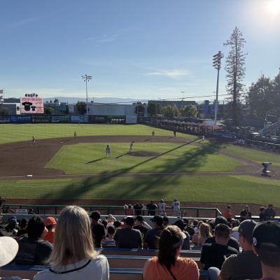 A minor-league baseball game in progress, seen from the stands with players on the infield