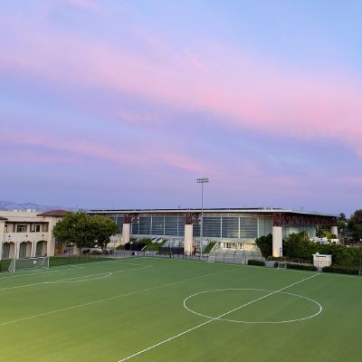 A soccer field at dusk under a pink sky, with the moon visible above a sports building