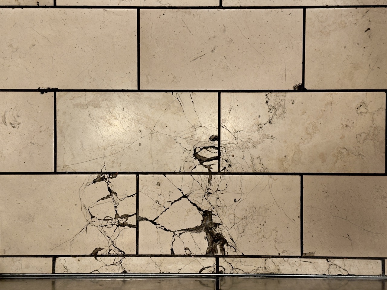 A floor of cream marble tiles laced with dark natural veining and fine cracks.