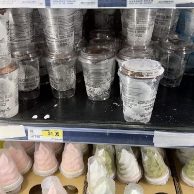 A grocery cooler shelf stacked with clear "Ice Cup (Big Ball)" cups, soft-serve cups on the shelf below and a $1.99 price tag.