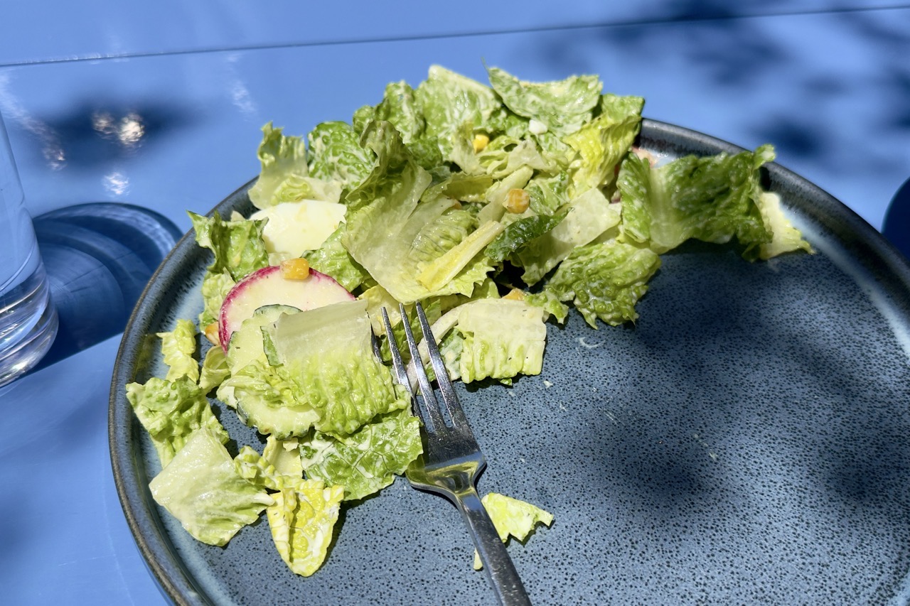 There is an egg in there amongst that salad, on a dark blue plate, on a lighter blue table.