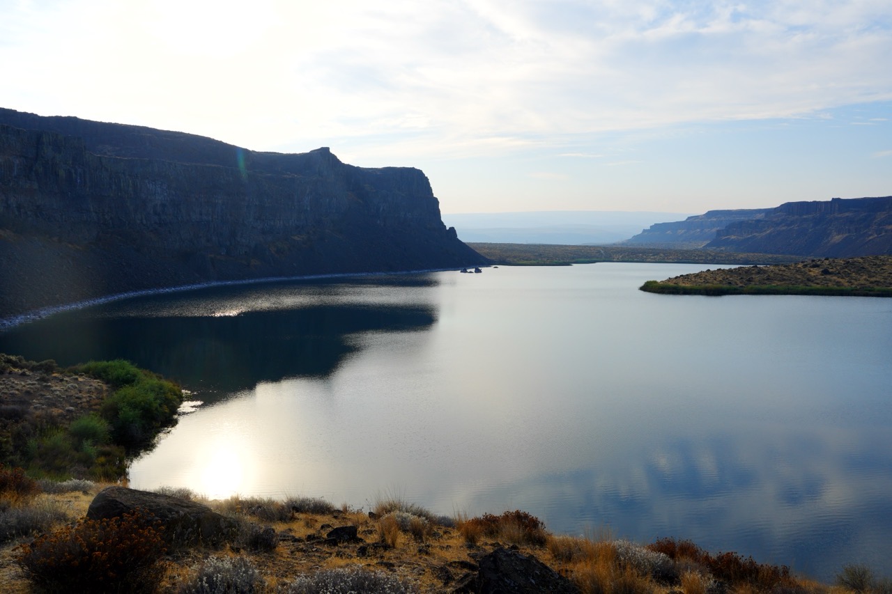 A still reservoir between steep basalt cliffs, with low sun reflecting on the calm water.