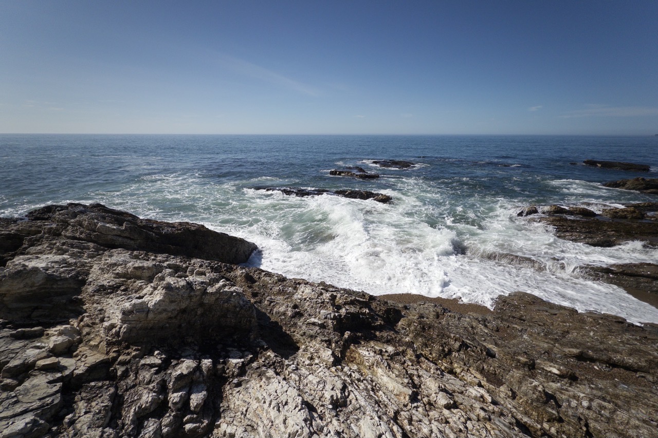 Sea foam churning over a rocky point, with calm blue ocean stretching to the horizon.