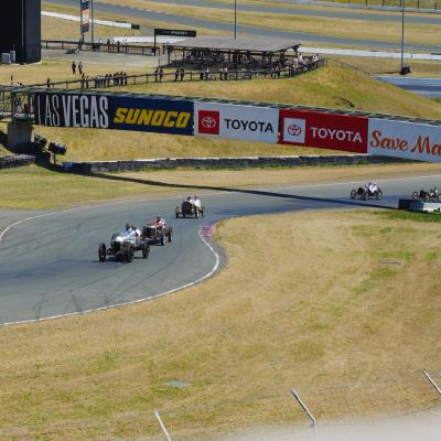Vintage open-wheel cars rounding a distant track turn below trackside Las Vegas, Sunoco and Toyota banners.