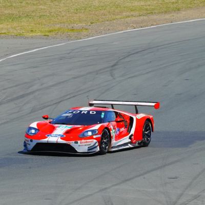 A red-and-white Ford GT race car cornering on an otherwise empty stretch of track.