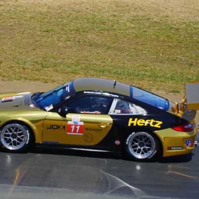 A gold-and-black Hertz-liveried Porsche 911, number 11, leaning through a corner.