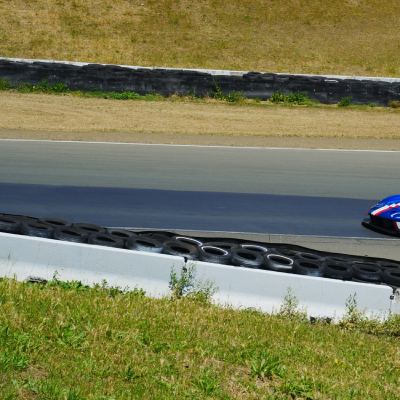 A blue-and-red prototype racer on the track, passing a tire-lined barrier on the hillside.