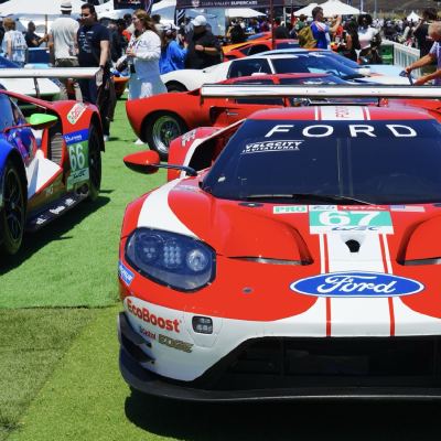 The nose of a red-and-white Ford GT, number 67, on display in the paddock among other GT cars and spectators.