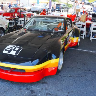 A black vintage race coupe with a red front air dam, number 49, parked in the paddock beside a number 48 car.