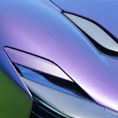 Close-up of a supercar's flank in colour-shifting purple-green paint, with a gold wheel and mesh side intakes.