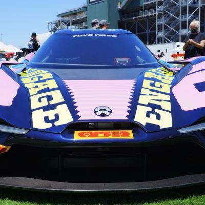Head-on view of a navy-and-pink 'ENGAGE'-liveried electric hypercar displayed on the grass, spectators behind.