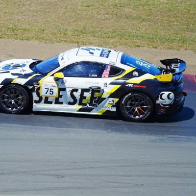 A white, yellow and black 'See See' Porsche Cayman, number 75, mid-corner.