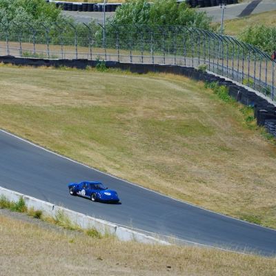 A vintage blue Ford GT40 trailed by a blue coupe along a downhill section of track.