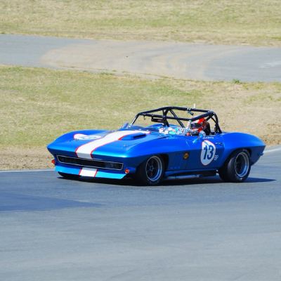 A blue Corvette Sting Ray roadster, number 13, leading an orange sports-racer, number 70, through a turn.
