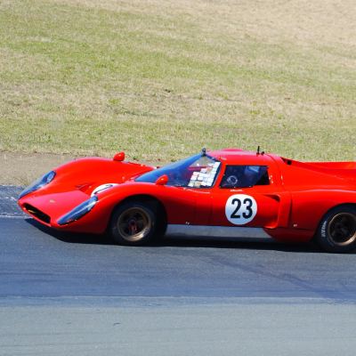 A red vintage sports-racing coupe, number 23, on the track in low sun.